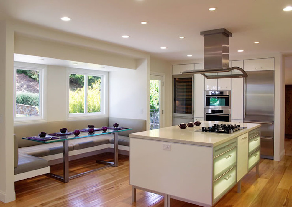 Expansive modern kitchen in San Francisco with flat-panel cabinets, white cabinets, stainless steel appliances, light hardwood floors and with island.