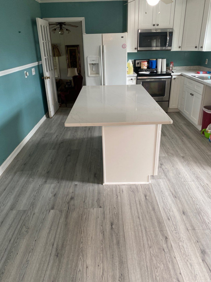 Example of a small l-shaped laminate floor and gray floor eat-in kitchen design with a drop-in sink, shaker cabinets, white cabinets, quartz countertops, stainless steel appliances, an island and white countertops