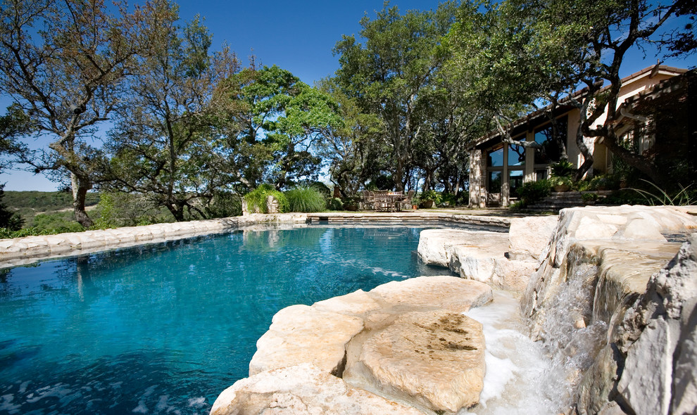 This is an example of a mid-sized traditional backyard custom-shaped natural pool in Austin with natural stone pavers and a hot tub.