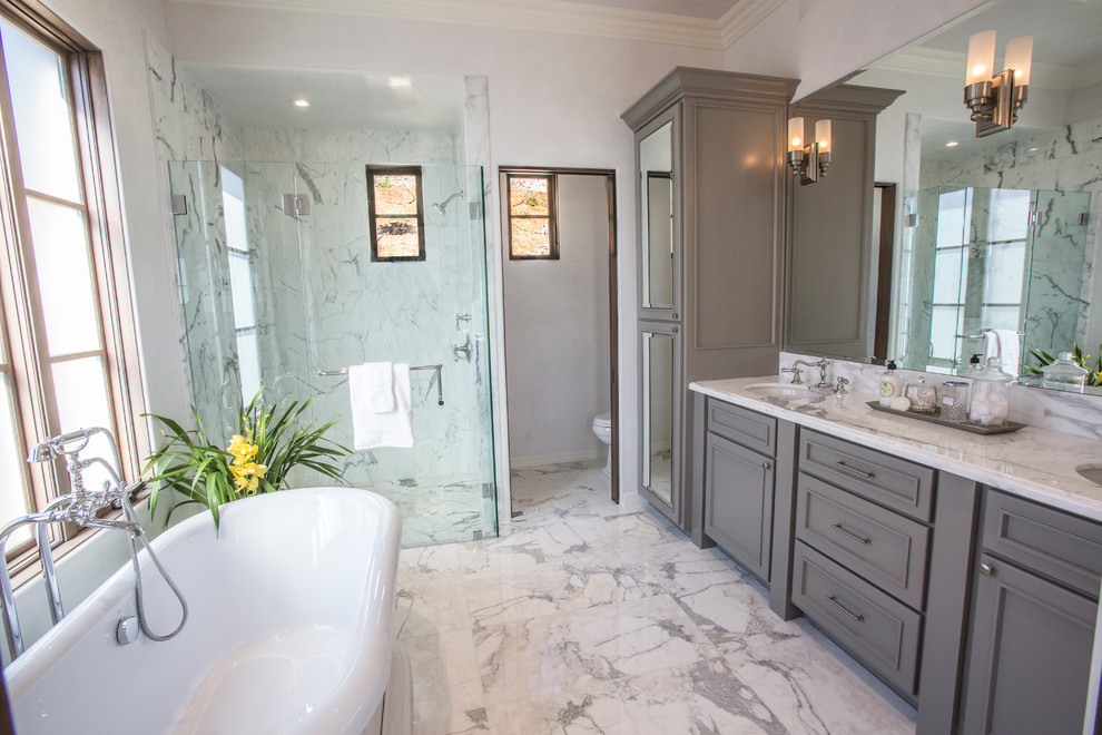 Inspiration for a mid-sized transitional master bathroom in Santa Barbara with recessed-panel cabinets, a freestanding tub, a one-piece toilet, white walls, marble floors, an undermount sink, marble benchtops, an alcove shower, brown cabinets, gray tile, marble, grey floor and a hinged shower door.