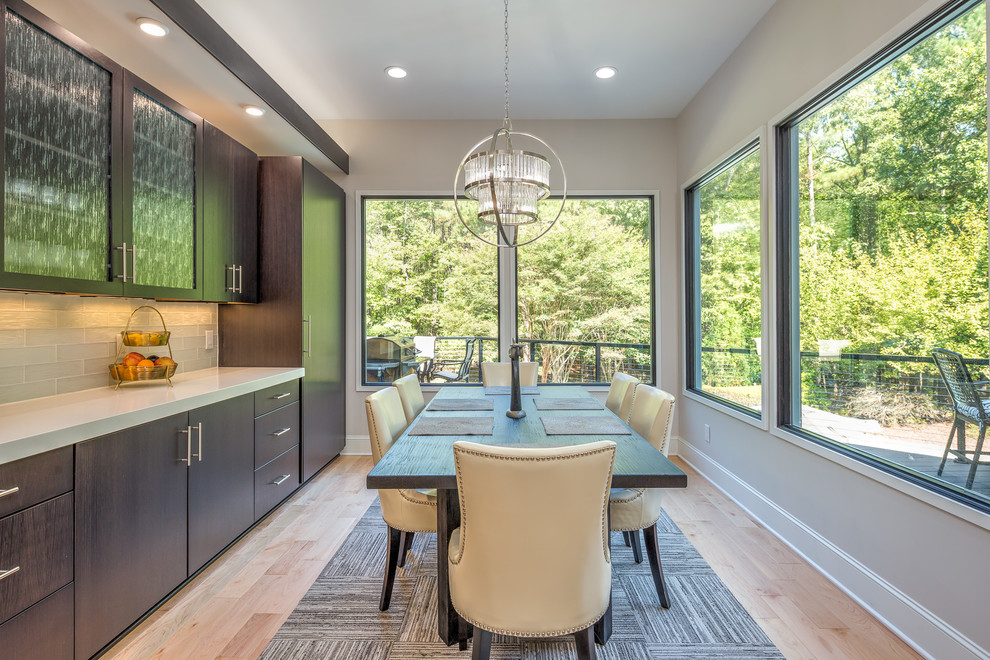 Photo of a large contemporary single-wall eat-in kitchen in Raleigh with an undermount sink, flat-panel cabinets, dark wood cabinets, quartz benchtops, white splashback, glass tile splashback, stainless steel appliances, light hardwood floors, with island and white benchtop.