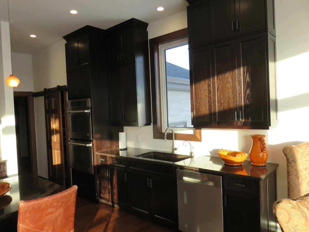 Large transitional l-shaped dark wood floor open concept kitchen photo with an undermount sink, recessed-panel cabinets, dark wood cabinets, quartz countertops, stainless steel appliances and an island
