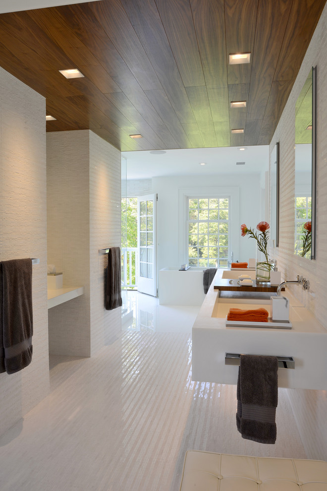 This is an example of a contemporary bathroom in New York with a trough sink, a freestanding tub, white tile and white walls.