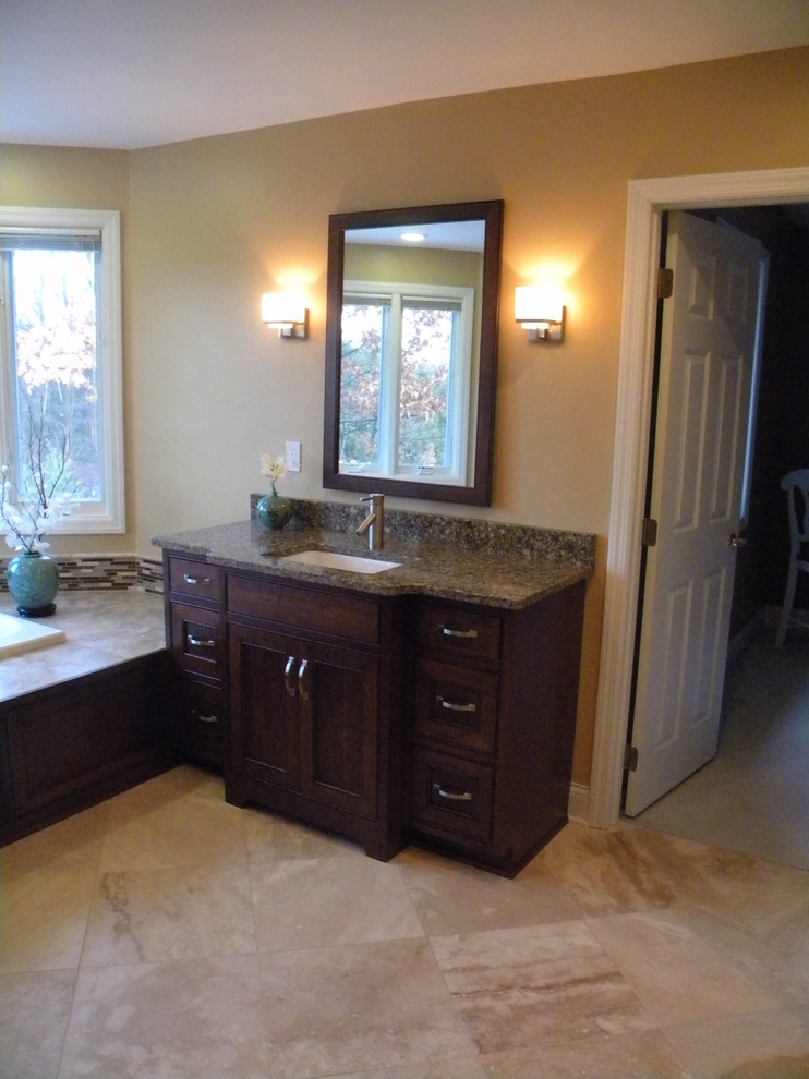 Large transitional master beige tile porcelain tile drop-in bathtub photo with an undermount sink, recessed-panel cabinets, dark wood cabinets, granite countertops, a two-piece toilet and beige walls