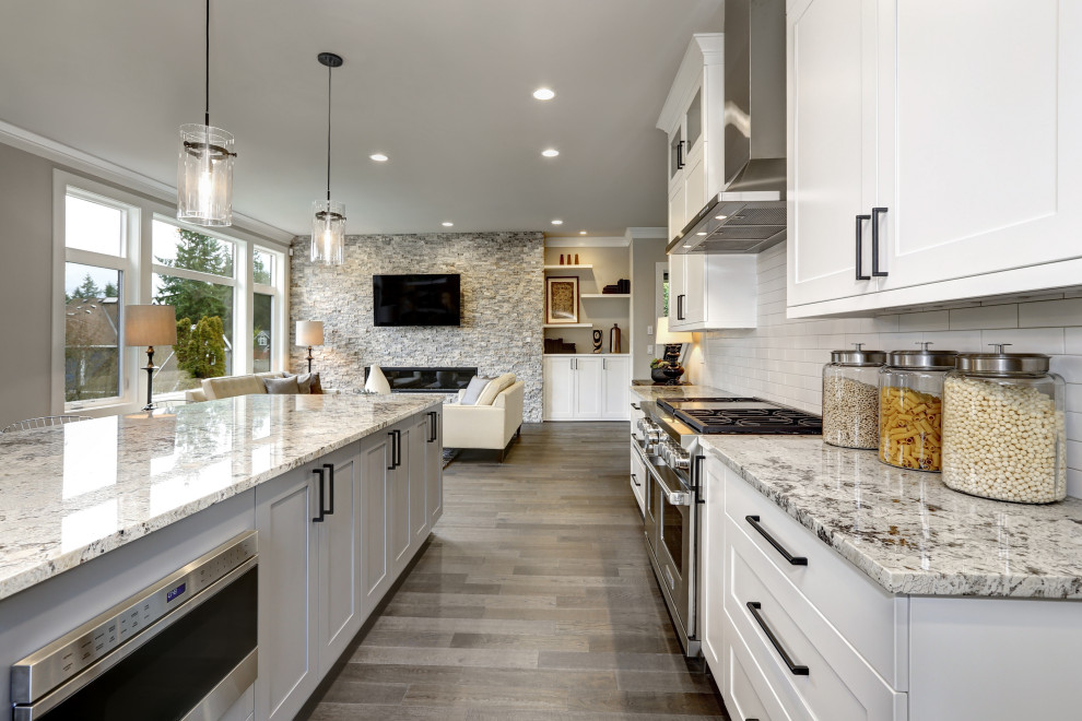 Example of a large transitional l-shaped medium tone wood floor and brown floor eat-in kitchen design in San Francisco with an undermount sink, shaker cabinets, white cabinets, granite countertops, white backsplash, stone tile backsplash, stainless steel appliances, an island and gray countertops