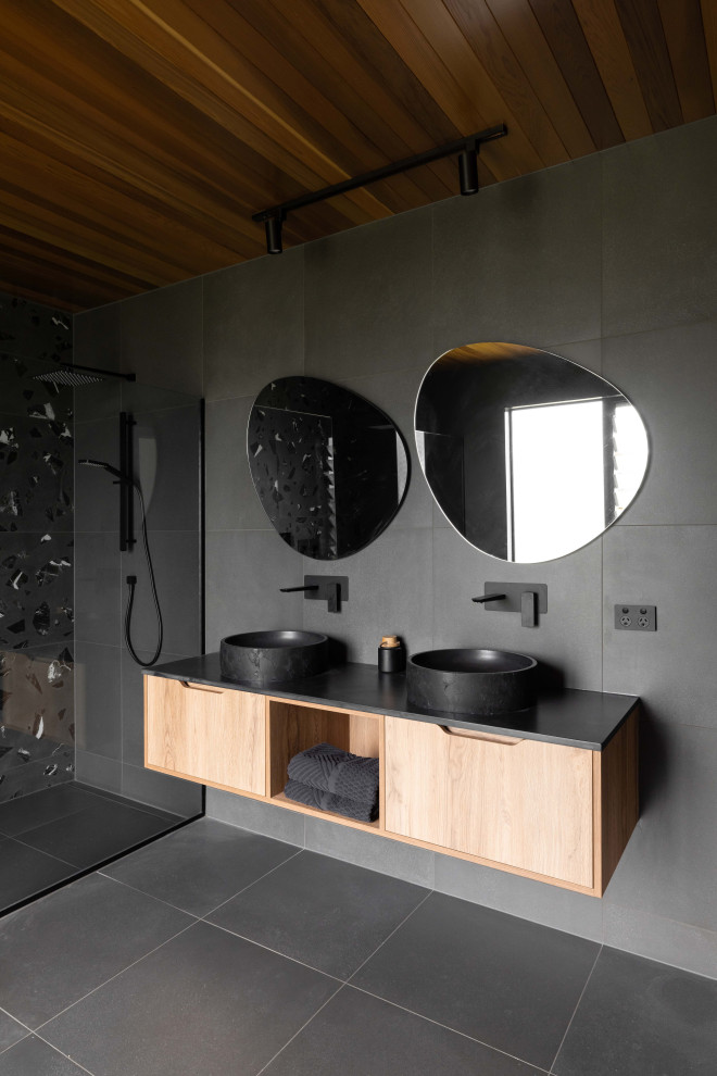 Large modern master bathroom in Auckland with flat-panel cabinets, light wood cabinets, a double shower, black tile, cement tile, cement tiles, a vessel sink, engineered quartz benchtops, a sliding shower screen, black benchtops, a double vanity, a floating vanity and timber.