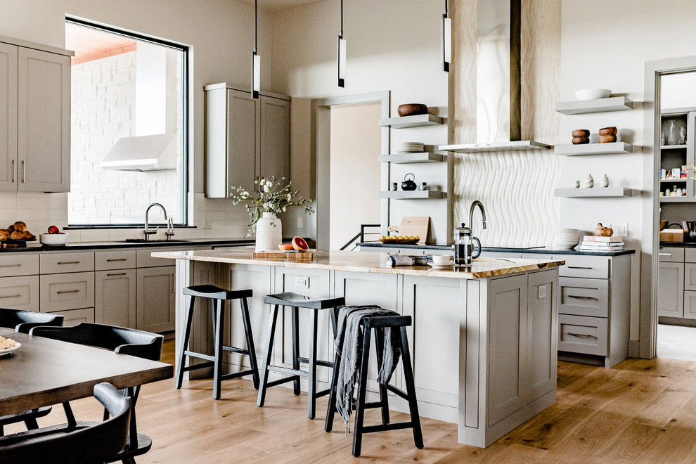 Inspiration for a mid-sized contemporary l-shaped eat-in kitchen in Austin with shaker cabinets, grey cabinets, granite benchtops, white splashback, ceramic splashback, with island, beige floor, an undermount sink, stainless steel appliances and light hardwood floors.