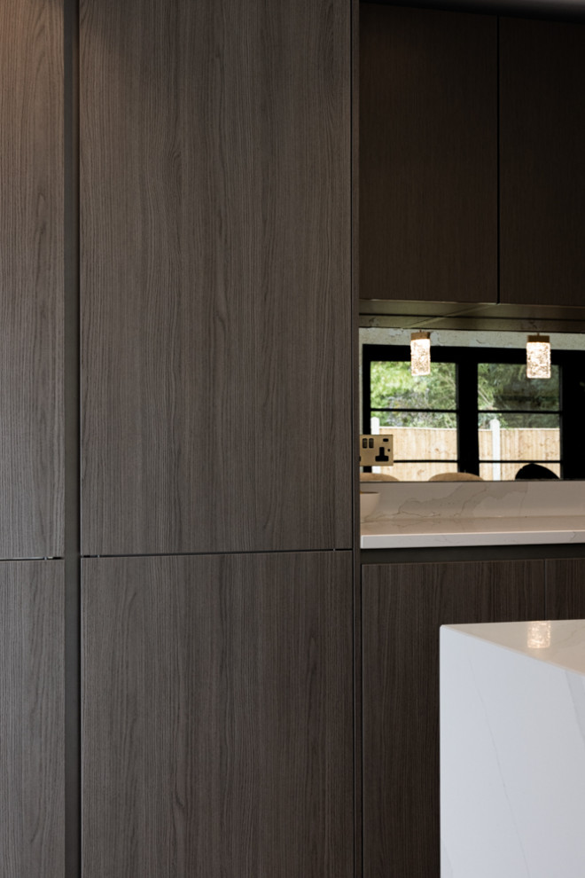 Mid-sized modern galley open plan kitchen in London with an integrated sink, flat-panel cabinets, dark wood cabinets, quartzite benchtops, metallic splashback, mirror splashback, stainless steel appliances, ceramic floors, a peninsula, beige floor and white benchtop.