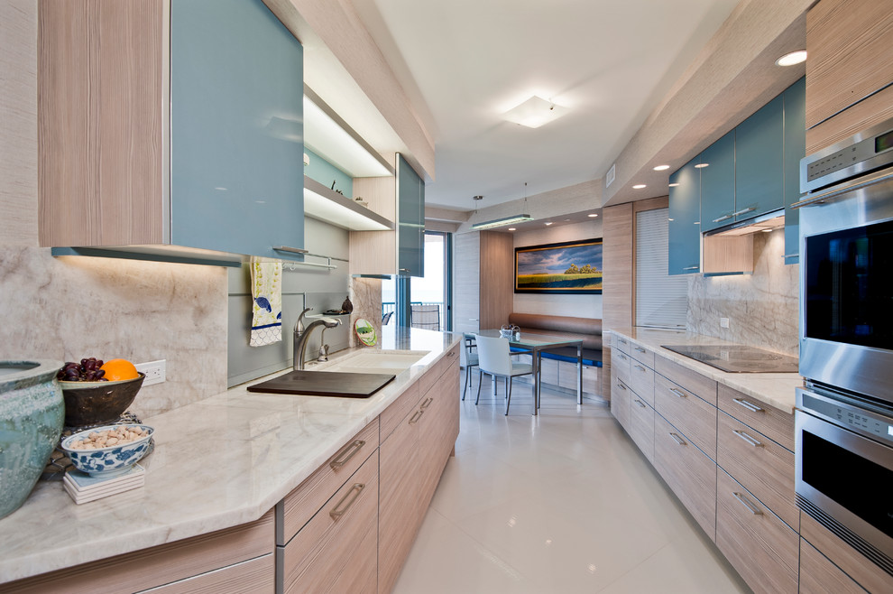 Contemporary galley separate kitchen in Miami with flat-panel cabinets, an undermount sink, blue cabinets, beige splashback, stone slab splashback and stainless steel appliances.