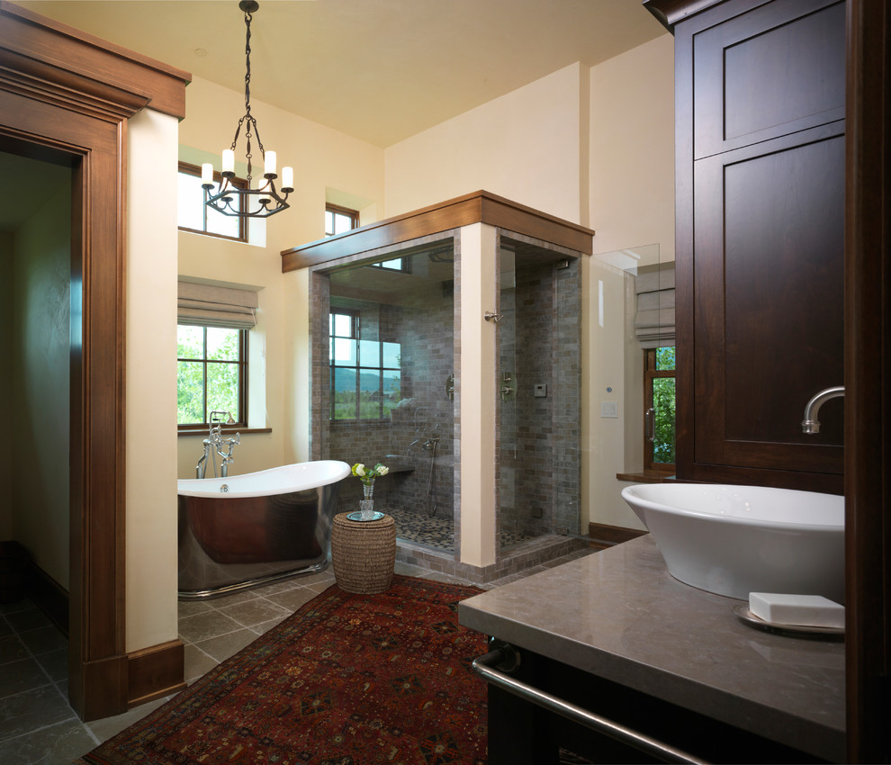 Freestanding bathtub - large rustic master gray tile and stone tile slate floor freestanding bathtub idea with beige walls, a vessel sink, shaker cabinets, dark wood cabinets and granite countertops