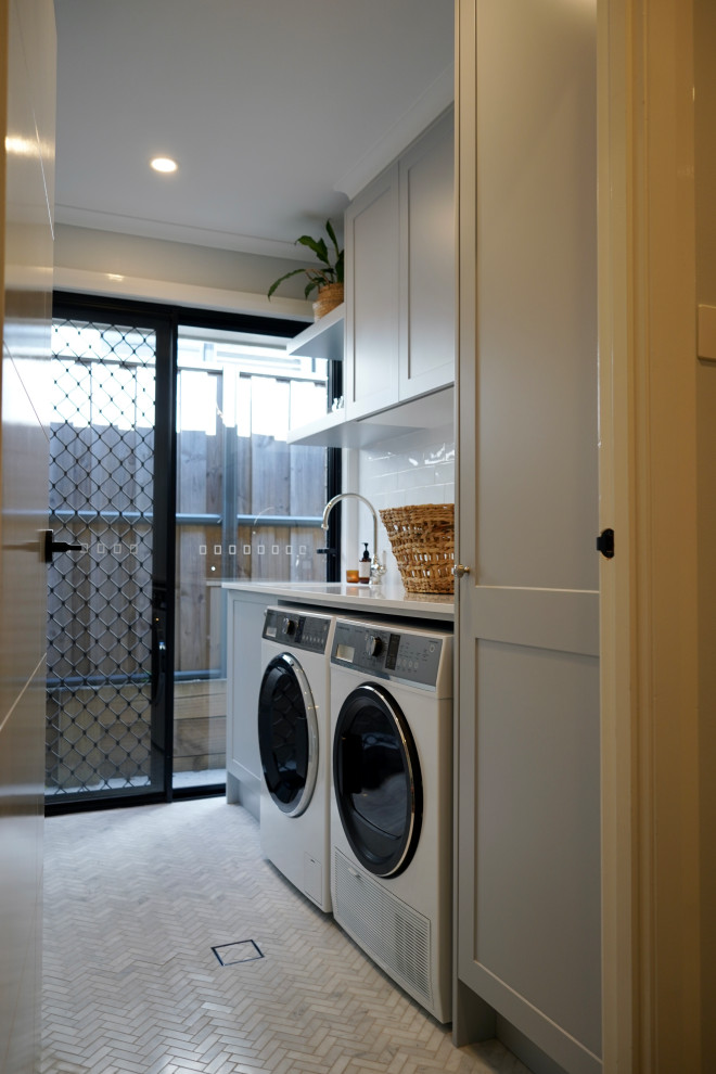 Inspiration for a small single-wall dedicated laundry room in Sydney with an undermount sink, shaker cabinets, grey cabinets, quartz benchtops, white splashback, subway tile splashback, white walls, marble floors, a side-by-side washer and dryer, grey floor and white benchtop.
