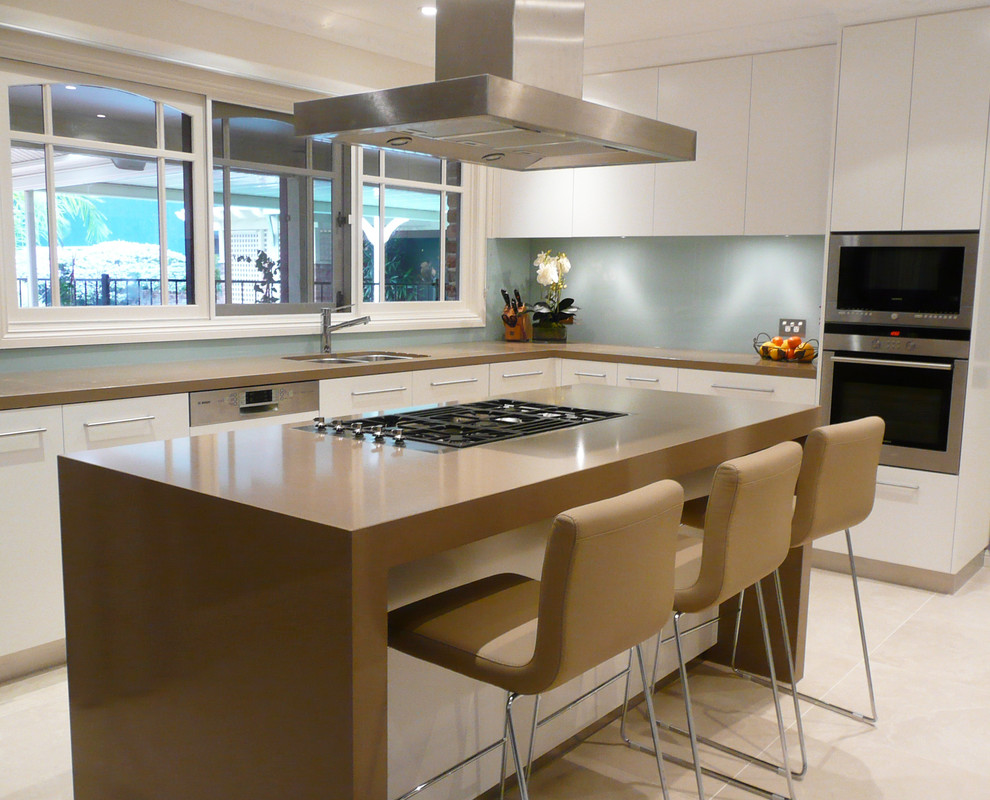 This is an example of a mid-sized contemporary l-shaped eat-in kitchen in Sydney with a double-bowl sink, flat-panel cabinets, white cabinets, quartz benchtops, blue splashback, glass sheet splashback, stainless steel appliances, cement tiles, with island and beige floor.