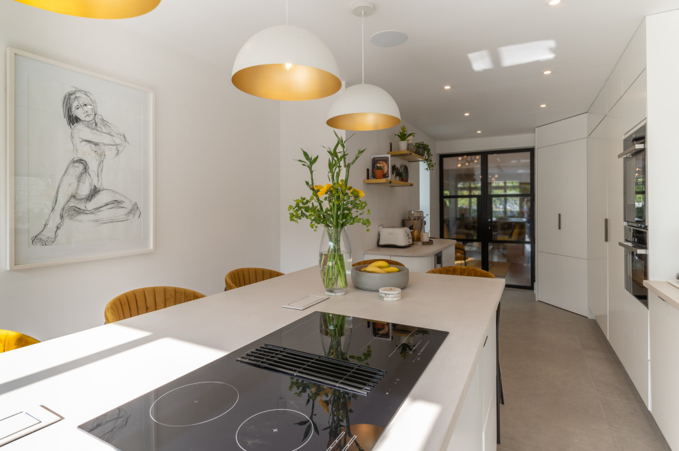 Large contemporary single-wall open plan kitchen in London with an integrated sink, flat-panel cabinets, white cabinets, black appliances, porcelain floors, multiple islands, grey floor and white benchtop.
