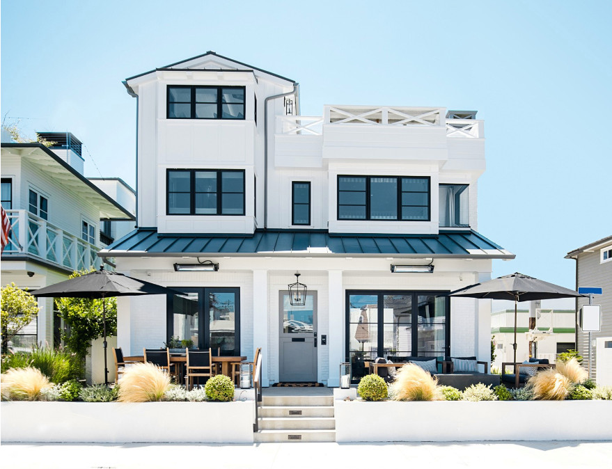 Photo of a large beach style two-storey white house exterior in Orange County with mixed siding, a gable roof and a metal roof.