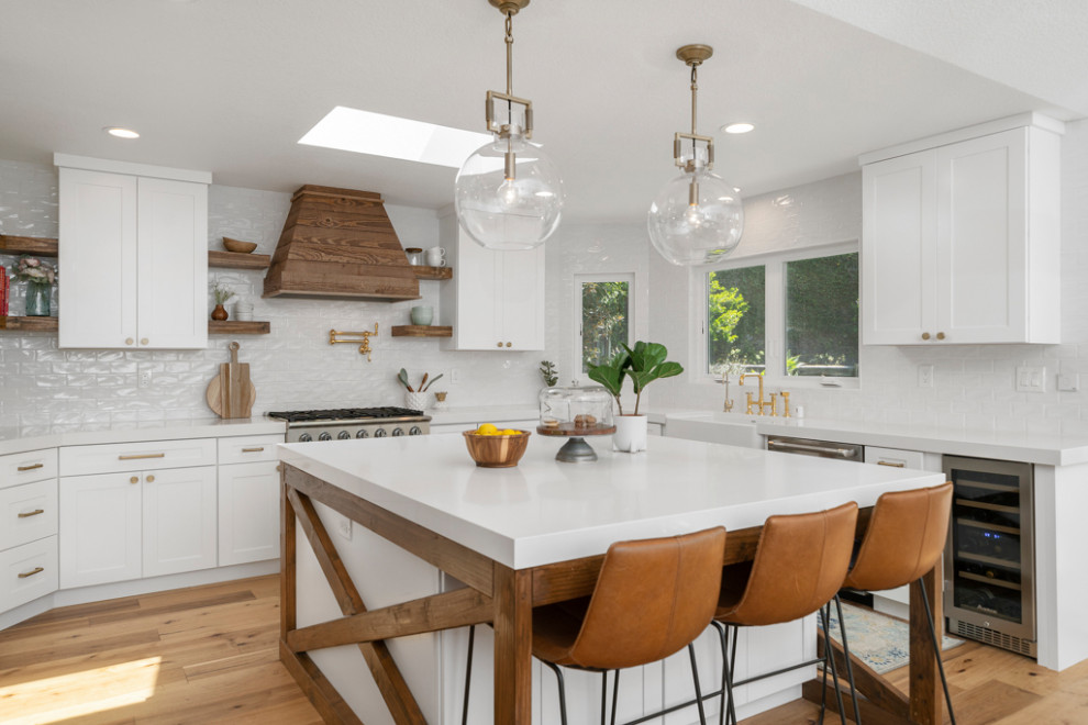 Inspiration for a large transitional u-shaped medium tone wood floor and brown floor eat-in kitchen remodel in Orange County with a farmhouse sink, shaker cabinets, white cabinets, quartz countertops, white backsplash, subway tile backsplash, stainless steel appliances, an island and white countertops