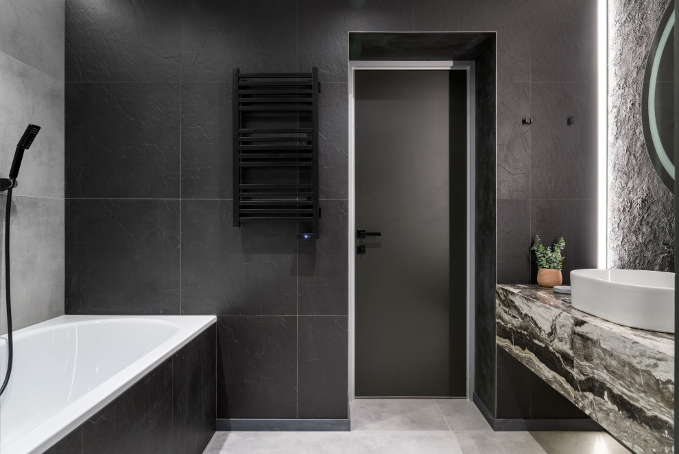 Идея дизайна: большая ванная комната в современном стиле с плоскими фасадами, серыми фасадами, полновстраиваемой ванной, душем в нише, инсталляцией, серой плиткой, керамогранитной плиткой, черными стенами, полом из керамогранита, душевой кабиной, накладной раковиной, столешницей из плитки, серым полом, душем с распашными дверями, серой столешницей, зеркалом с подсветкой, тумбой под одну раковину и подвесной тумбой