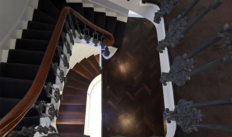 Large traditional wood curved staircase in London with wood risers and metal railing.