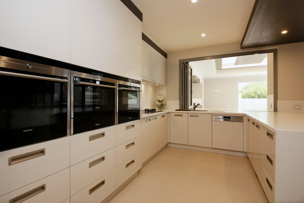 Large contemporary u-shaped kitchen pantry in Perth with a drop-in sink, solid surface benchtops, white splashback, stainless steel appliances, porcelain floors and with island.