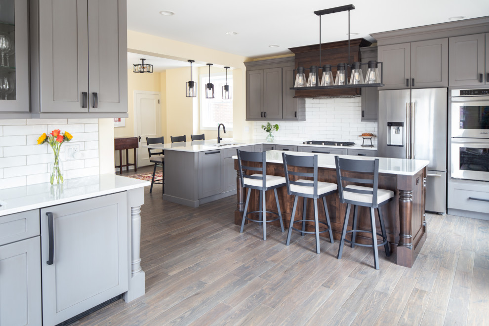 Kitchen - transitional medium tone wood floor and brown floor kitchen idea with an undermount sink, shaker cabinets, gray cabinets, quartz countertops, white backsplash, subway tile backsplash, stainless steel appliances, an island and white countertops