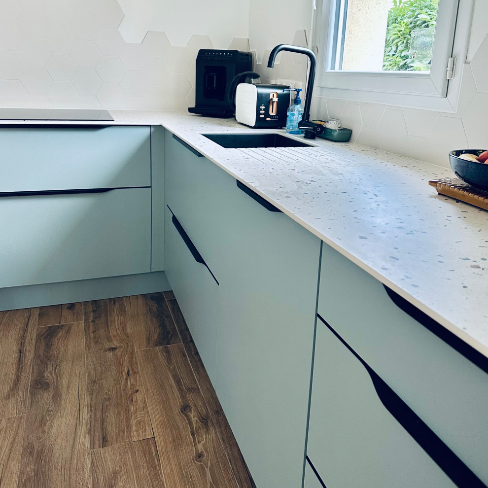 Example of a mid-sized minimalist l-shaped light wood floor and brown floor open concept kitchen design in Nantes with an undermount sink, blue cabinets, terrazzo countertops, beige backsplash, ceramic backsplash, black appliances, an island and blue countertops