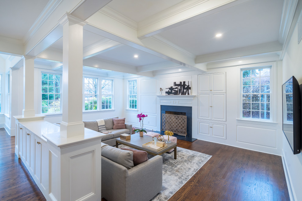 This is an example of a large transitional open concept family room in Philadelphia with white walls, dark hardwood floors, a standard fireplace, a wood fireplace surround, a wall-mounted tv, brown floor, coffered and panelled walls.
