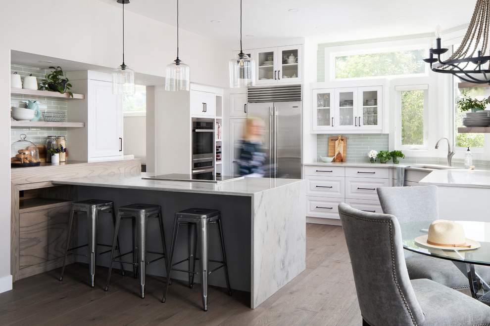 This is an example of a mid-sized transitional l-shaped eat-in kitchen in Calgary with an undermount sink, raised-panel cabinets, white cabinets, grey splashback, glass tile splashback, stainless steel appliances, dark hardwood floors, a peninsula, brown floor and grey benchtop.