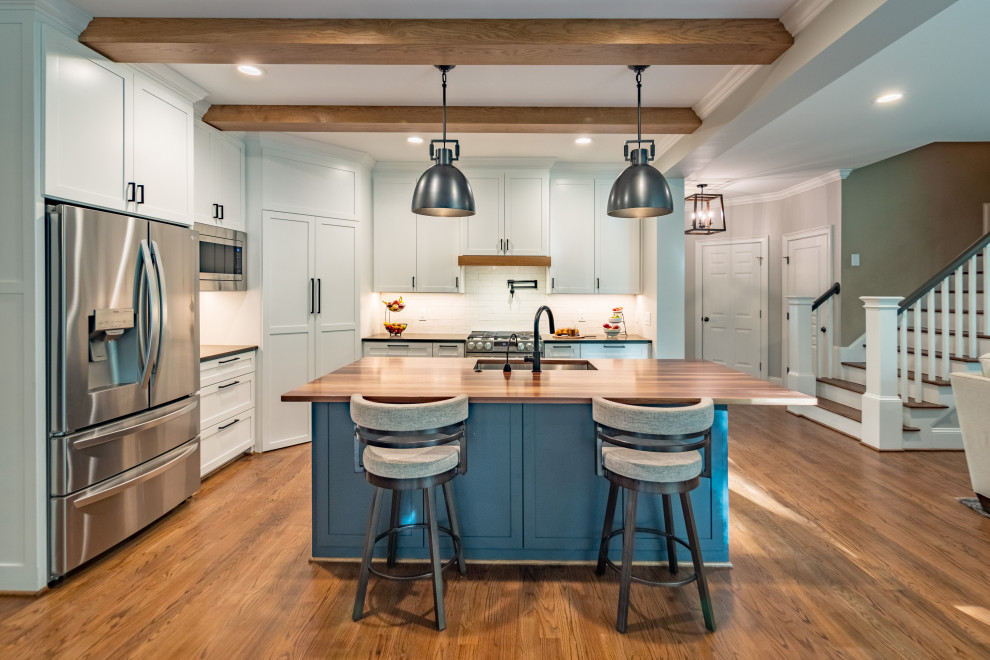 Large transitional exposed beam eat-in kitchen photo in Raleigh with shaker cabinets, white cabinets, wood countertops, white backsplash, subway tile backsplash and an island