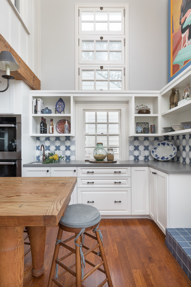 Design ideas for a mid-sized beach style l-shaped kitchen in San Diego with a single-bowl sink, white cabinets, quartz benchtops, multi-coloured splashback, terra-cotta splashback, stainless steel appliances, medium hardwood floors, grey benchtop and with island.