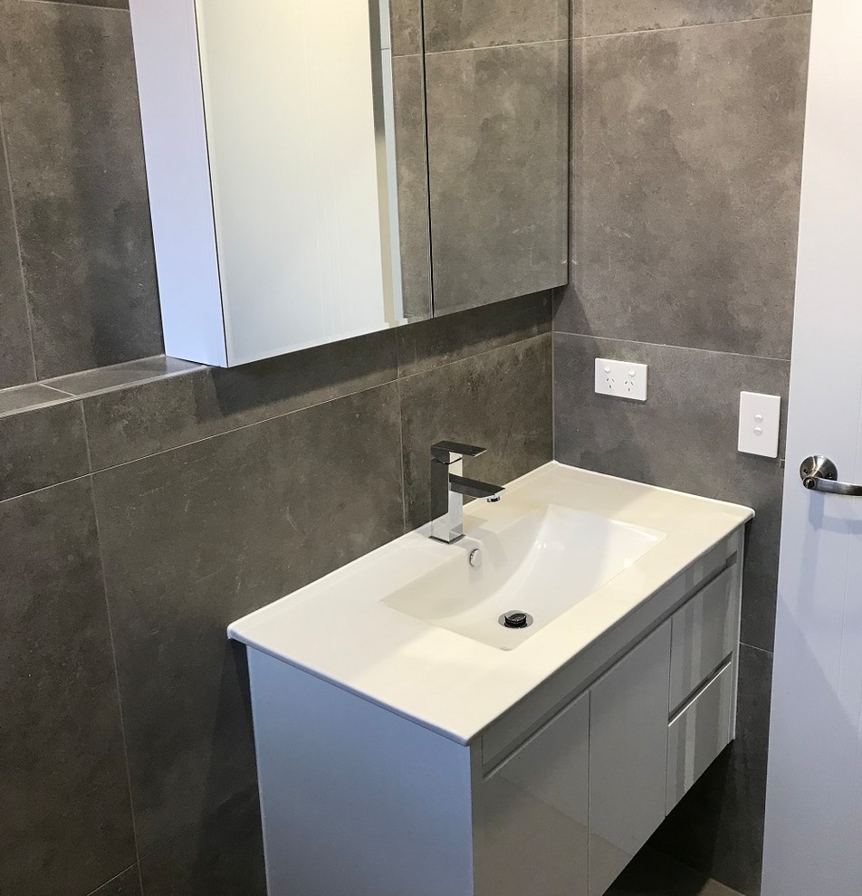 Photo of a mid-sized industrial bathroom in Sydney with a one-piece toilet, gray tile, porcelain tile, grey walls, porcelain floors, a wall-mount sink and grey floor.