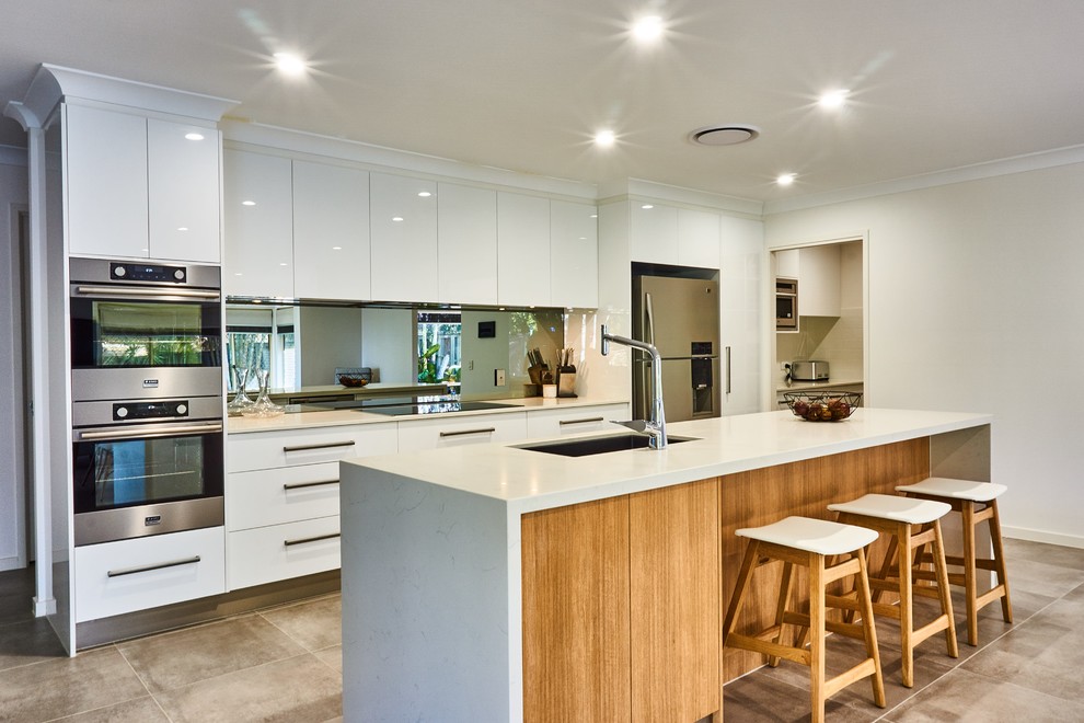 Photo of a mid-sized contemporary galley open plan kitchen in Gold Coast - Tweed with an undermount sink, flat-panel cabinets, white cabinets, mirror splashback, stainless steel appliances, with island, beige floor, white benchtop, quartz benchtops and metallic splashback.
