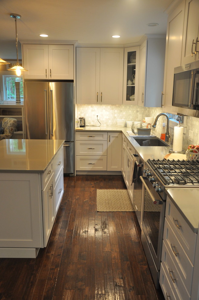 Example of a small transitional l-shaped dark wood floor and brown floor eat-in kitchen design in Boston with an undermount sink, recessed-panel cabinets, white cabinets, quartz countertops, white backsplash, porcelain backsplash, stainless steel appliances, an island and gray countertops