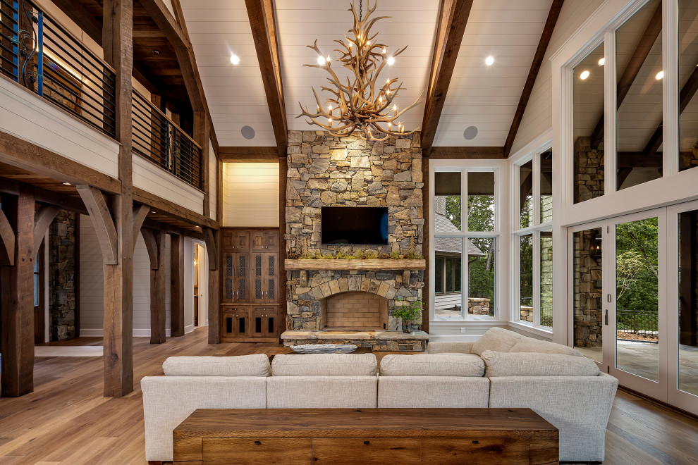 Large arts and crafts open concept family room in Other with beige walls, medium hardwood floors, a standard fireplace, a stone fireplace surround, grey floor, exposed beam and planked wall panelling.
