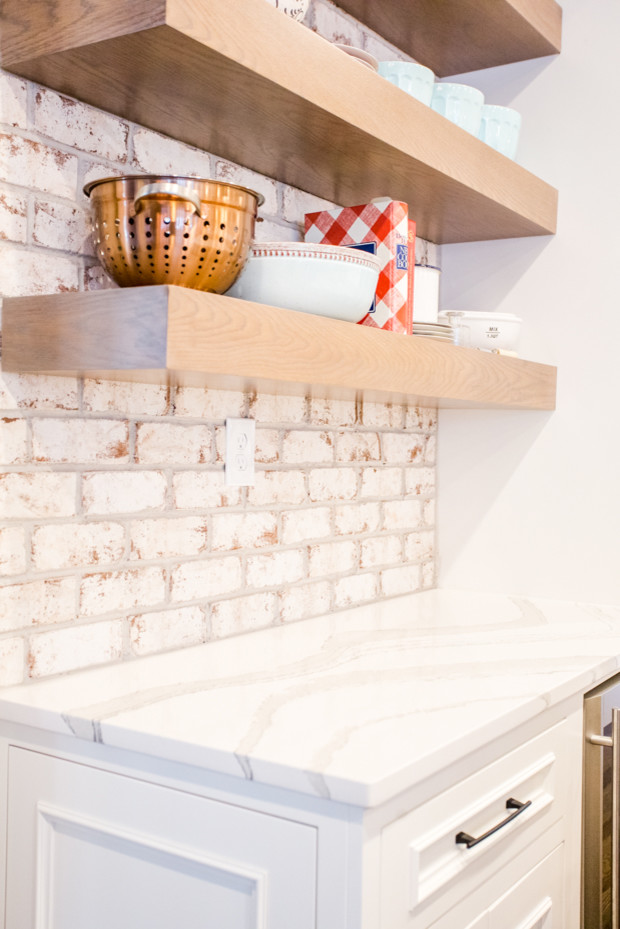Large transitional u-shaped medium tone wood floor and brown floor eat-in kitchen photo in Atlanta with a farmhouse sink, raised-panel cabinets, white cabinets, quartz countertops, white backsplash, brick backsplash, stainless steel appliances, an island and white countertops