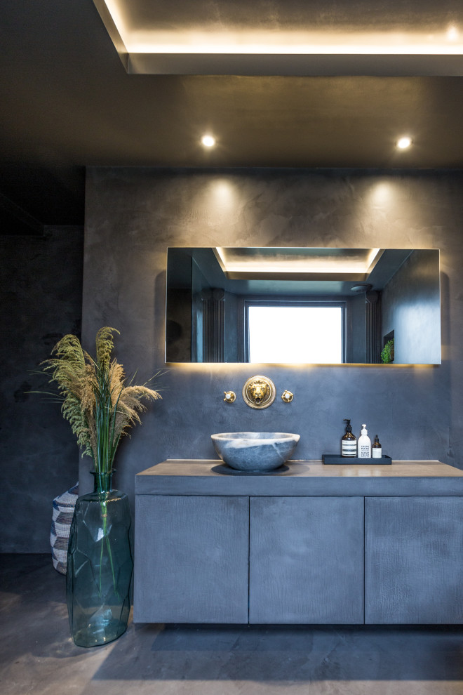 Design ideas for a mid-sized traditional master bathroom in London with flat-panel cabinets, black cabinets, a freestanding tub, a corner shower, a wall-mount toilet, black tile, black walls, concrete floors, a vessel sink, concrete benchtops, black floor, an open shower and black benchtops.