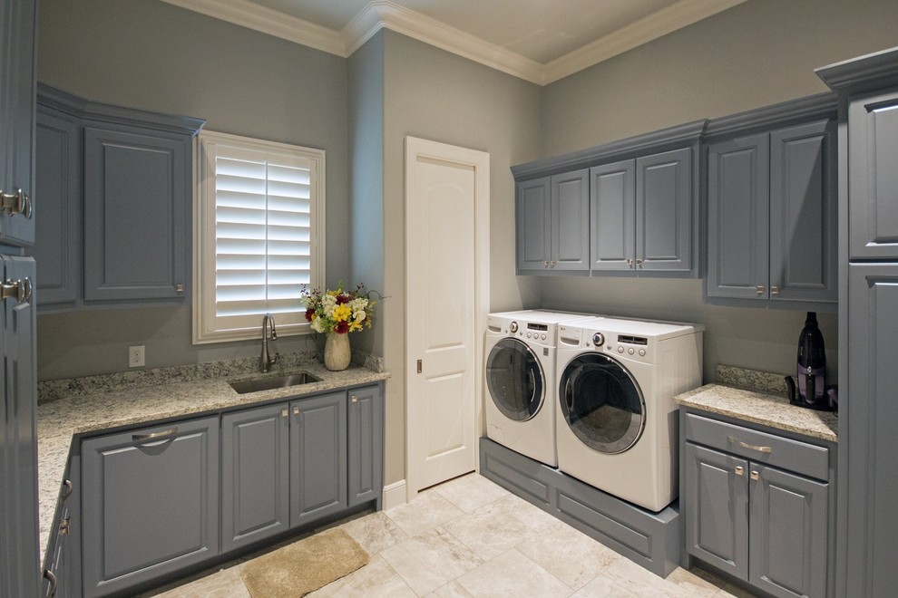 This is an example of a large transitional u-shaped utility room in Dallas with an undermount sink, raised-panel cabinets, grey cabinets, granite benchtops, grey walls, ceramic floors, a side-by-side washer and dryer and beige floor.