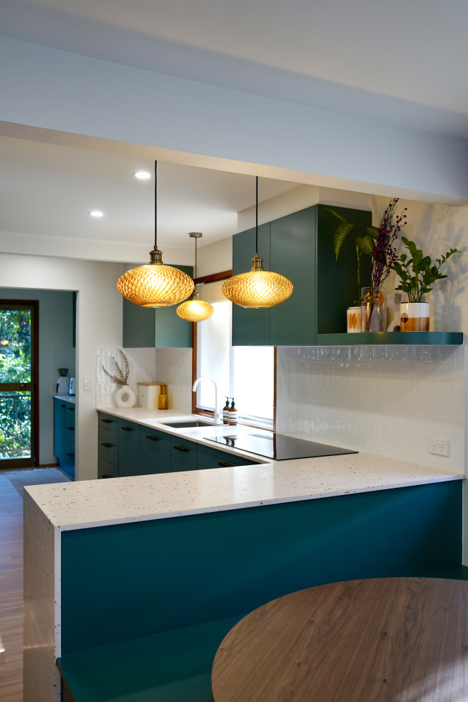 Photo of a large transitional galley open plan kitchen in Sydney with an undermount sink, flat-panel cabinets, green cabinets, terrazzo benchtops, white splashback, subway tile splashback, black appliances, light hardwood floors, with island, brown floor and multi-coloured benchtop.