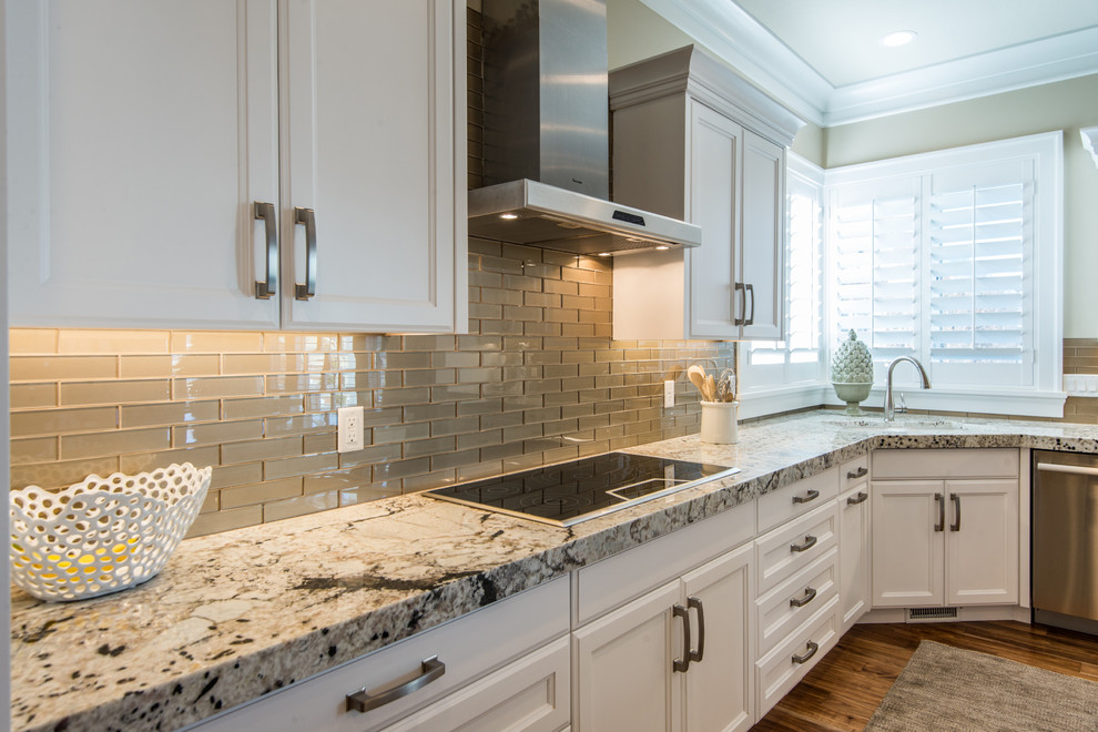 Inspiration for a mid-sized arts and crafts l-shaped open plan kitchen in Salt Lake City with an undermount sink, white cabinets, granite benchtops, metallic splashback, glass tile splashback, stainless steel appliances, medium hardwood floors, with island and raised-panel cabinets.