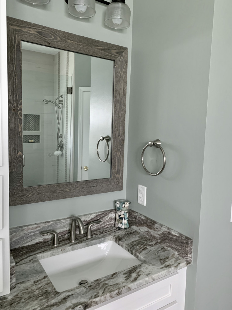 This is an example of a mid-sized beach style master bathroom in Other with shaker cabinets, white cabinets, a drop-in tub, a corner shower, white tile, ceramic tile, blue walls, vinyl floors, an undermount sink, marble benchtops, grey floor, a hinged shower door and multi-coloured benchtops.