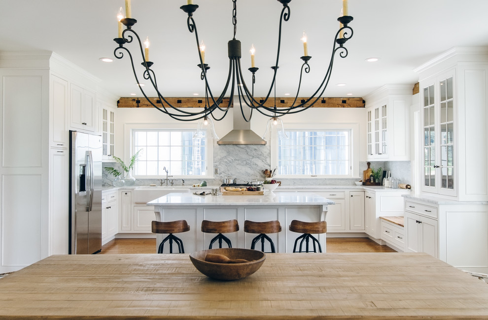 This is an example of a large country u-shaped eat-in kitchen in New York with a farmhouse sink, beaded inset cabinets, white cabinets, marble benchtops, white splashback, stone slab splashback, stainless steel appliances, medium hardwood floors and with island.