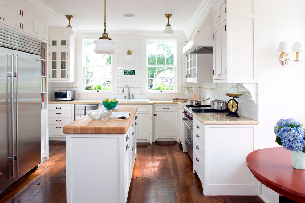 Inspiration for a mid-sized country u-shaped kitchen in Boston with a drop-in sink, shaker cabinets, white cabinets, white splashback, subway tile splashback, stainless steel appliances, with island, tile benchtops, dark hardwood floors and brown floor.