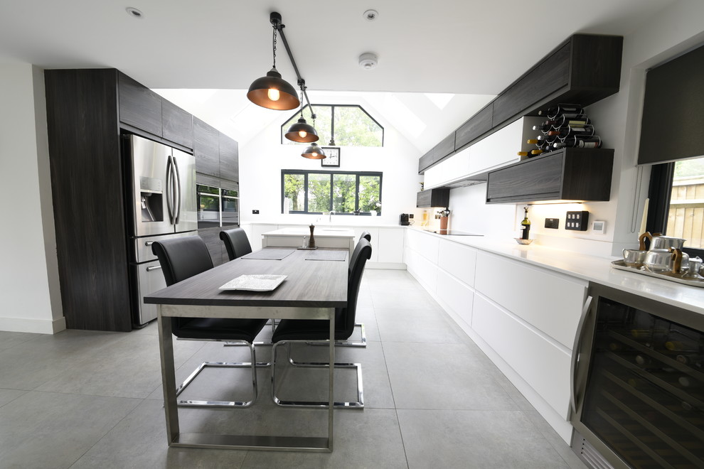 Large modern u-shaped eat-in kitchen in Kent with a drop-in sink, flat-panel cabinets, white cabinets, solid surface benchtops, white splashback, panelled appliances, porcelain floors, with island and grey floor.