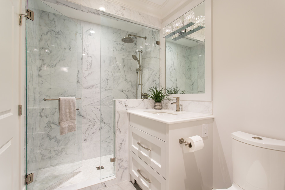 This is an example of a small transitional master bathroom in Vancouver with shaker cabinets, grey cabinets, a drop-in tub, an alcove shower, a wall-mount toilet, gray tile, marble, grey walls, porcelain floors, a drop-in sink, engineered quartz benchtops, grey floor, a hinged shower door and white benchtops.