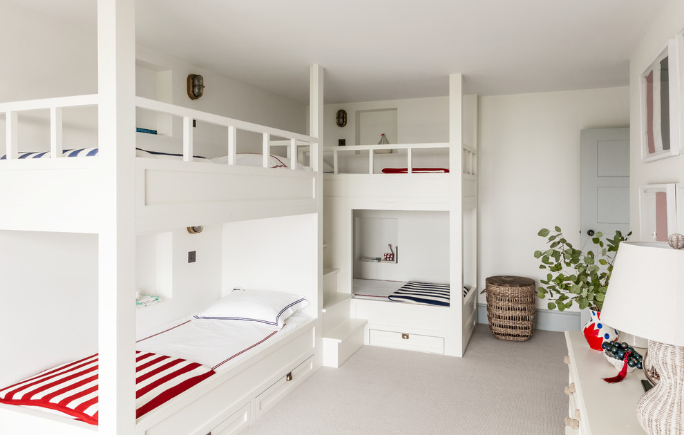 This is an example of a mid-sized beach style gender-neutral kids' bedroom for kids 4-10 years old in Sussex with white walls, carpet and beige floor.