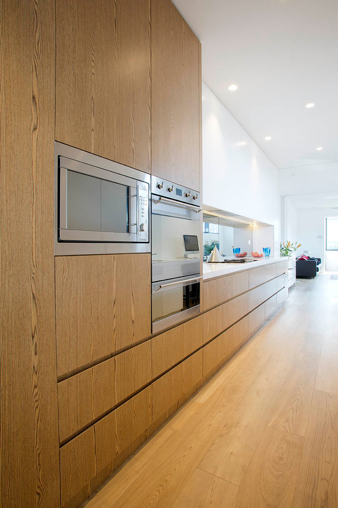 Large contemporary galley kitchen pantry in Sydney with a drop-in sink, solid surface benchtops, mirror splashback, stainless steel appliances, medium hardwood floors and no island.