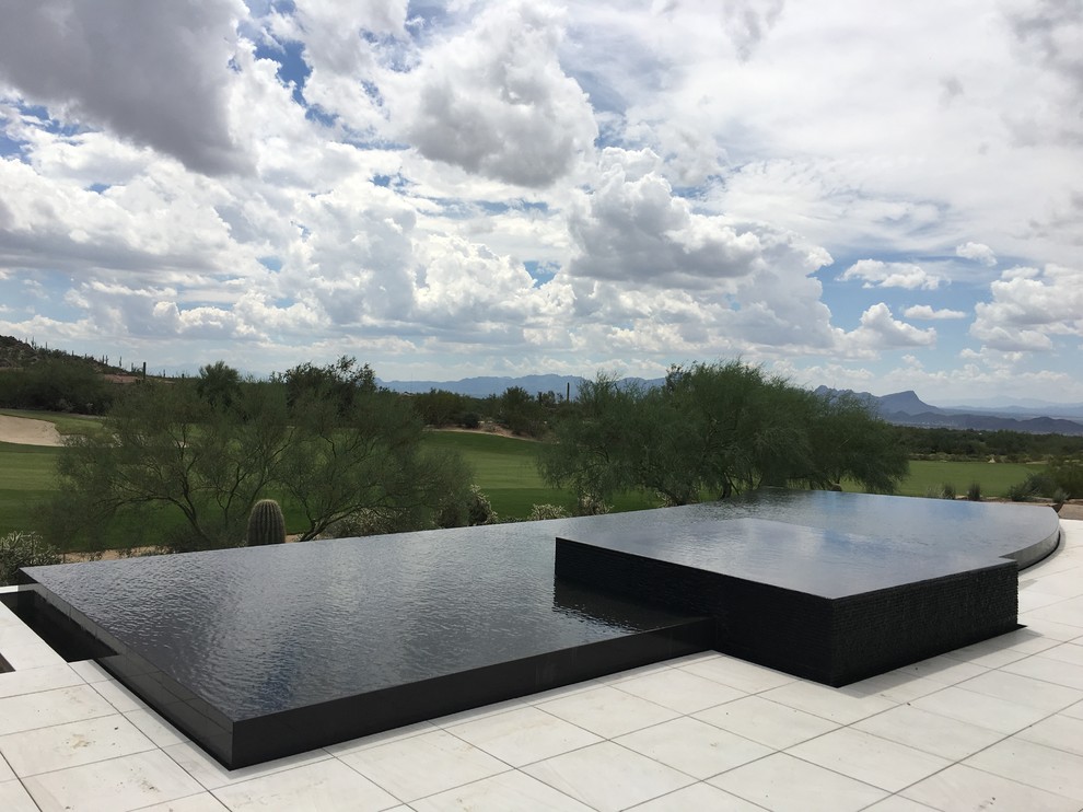 Photo of a large contemporary backyard custom-shaped infinity pool in Phoenix with a water feature and tile.