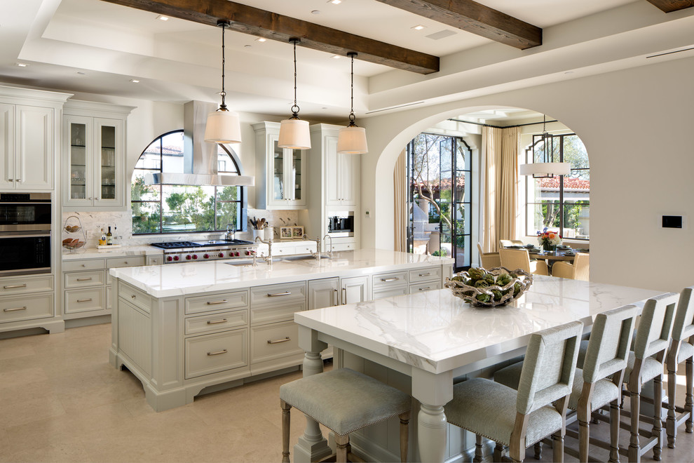 Photo of a mediterranean galley kitchen in Orange County with an undermount sink, recessed-panel cabinets, grey cabinets, multiple islands, beige floor and white benchtop.