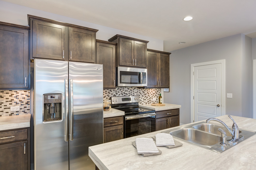 Mid-sized transitional galley kitchen photo with a double-bowl sink, recessed-panel cabinets, dark wood cabinets, laminate countertops, multicolored backsplash, ceramic backsplash, stainless steel appliances and an island