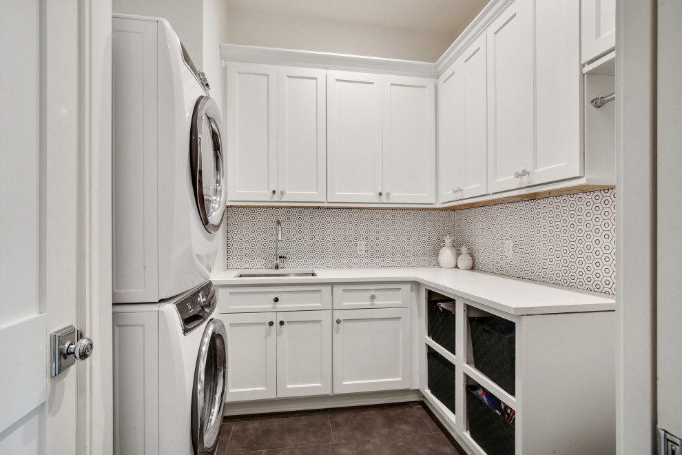 Photo of a small transitional u-shaped dedicated laundry room in New Orleans with an undermount sink, shaker cabinets, white cabinets, quartzite benchtops, white splashback, mosaic tile splashback, white walls, medium hardwood floors, a stacked washer and dryer, brown floor, white benchtop and vaulted.