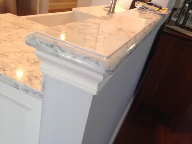 Mid-sized transitional l-shaped medium tone wood floor home design photo in Providence with a farmhouse sink, recessed-panel cabinets, white cabinets, solid surface countertops, white backsplash, glass tile backsplash, stainless steel appliances and a peninsula