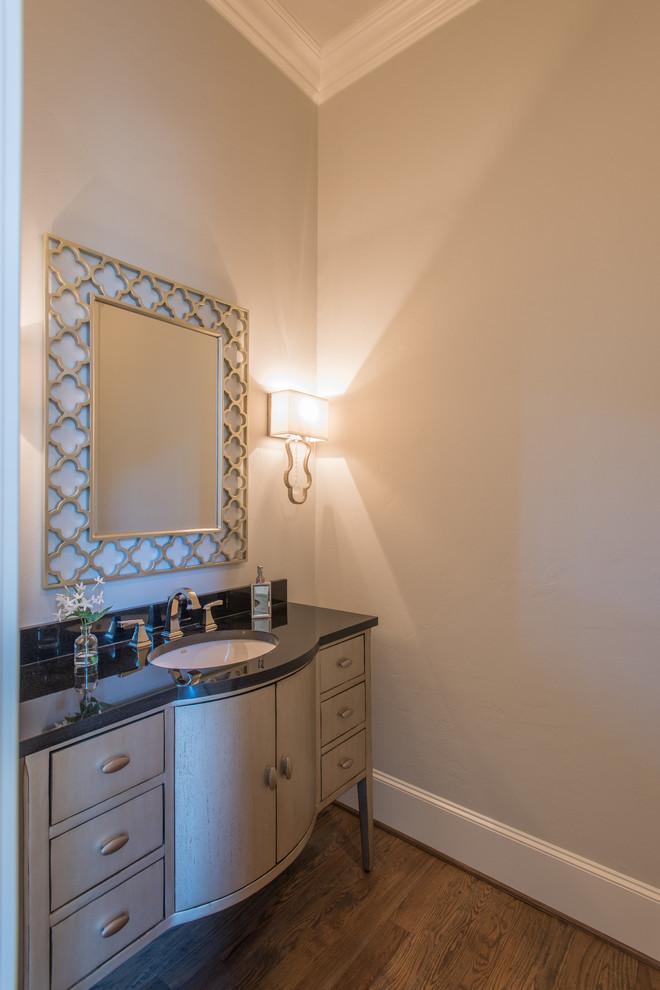 Photo of a mid-sized mediterranean powder room in Dallas with grey cabinets, grey walls, medium hardwood floors, an undermount sink, granite benchtops and brown floor.